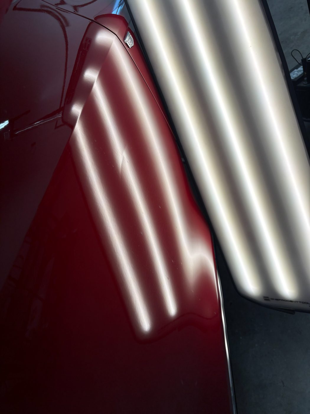 Reflection lines running straight across the red Cadillac panel after paintless dent repair