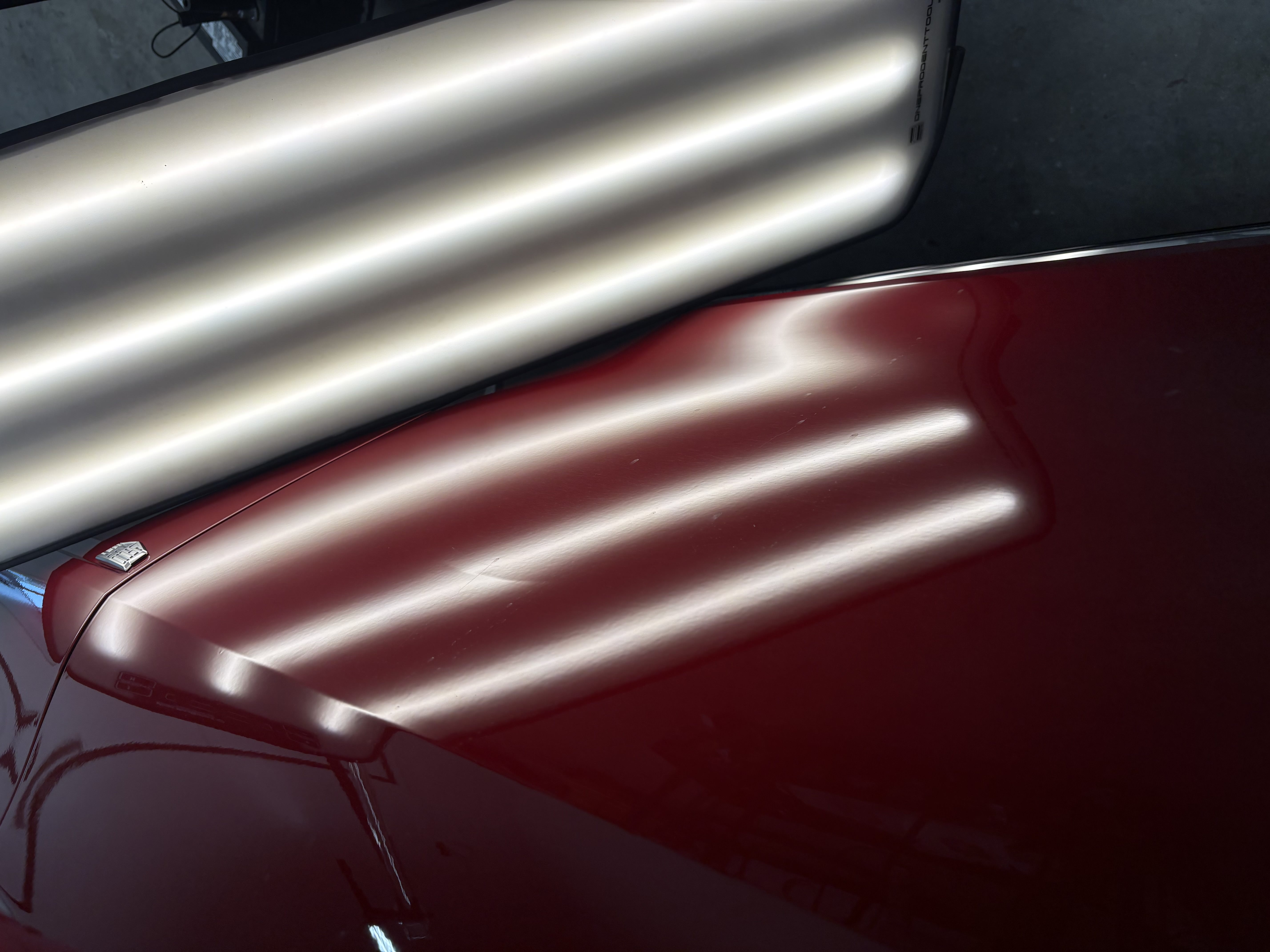 Paintless dent repair on a red Cadillac, reflection lines running straight after the pull